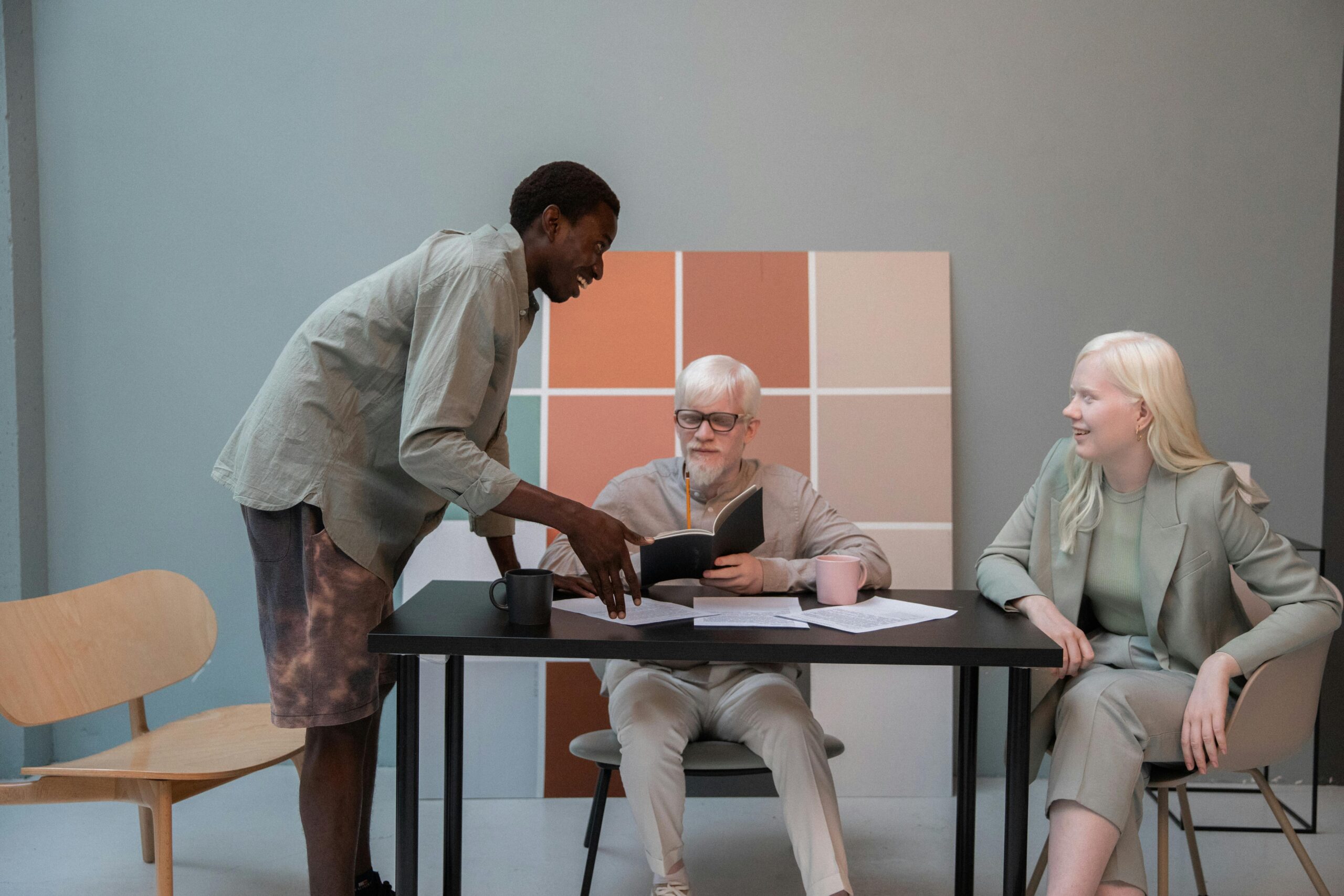 Group of multiethnic coworkers in casual clothes gathering around table with documents and talking about new project while working in modern office